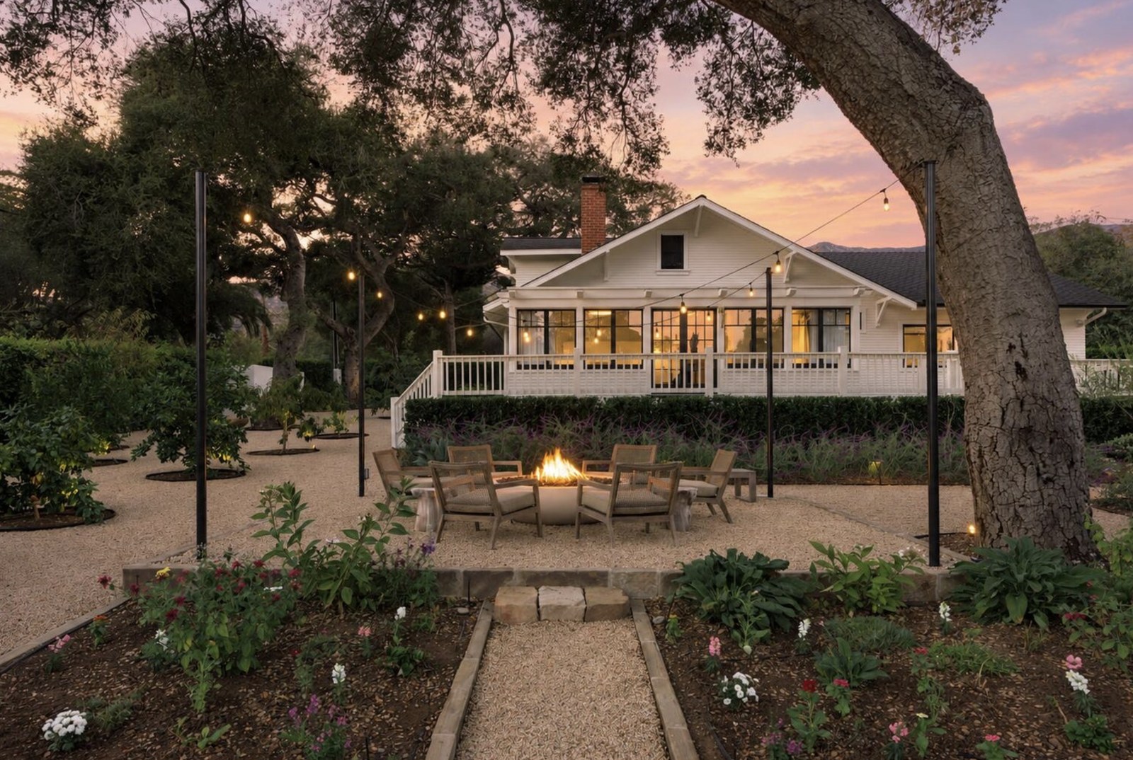 Farmhouse at 540 El Bosque Road at dusk, with a fire pit under the oaks and string lights through the trees