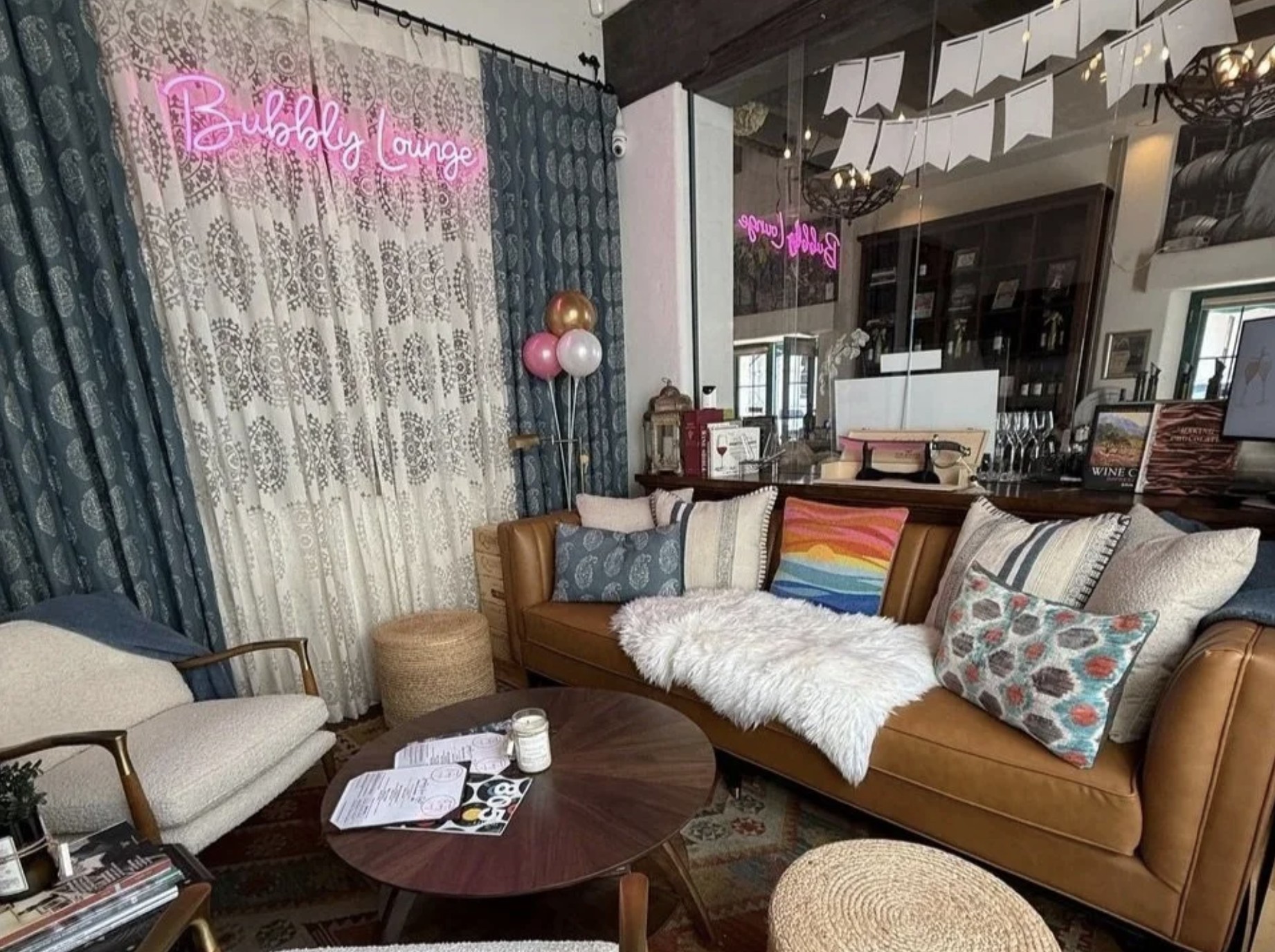 The lounge at Santa Barbara Bubbly Lounge, with a pink neon sign, a leather couch, and patterned curtains